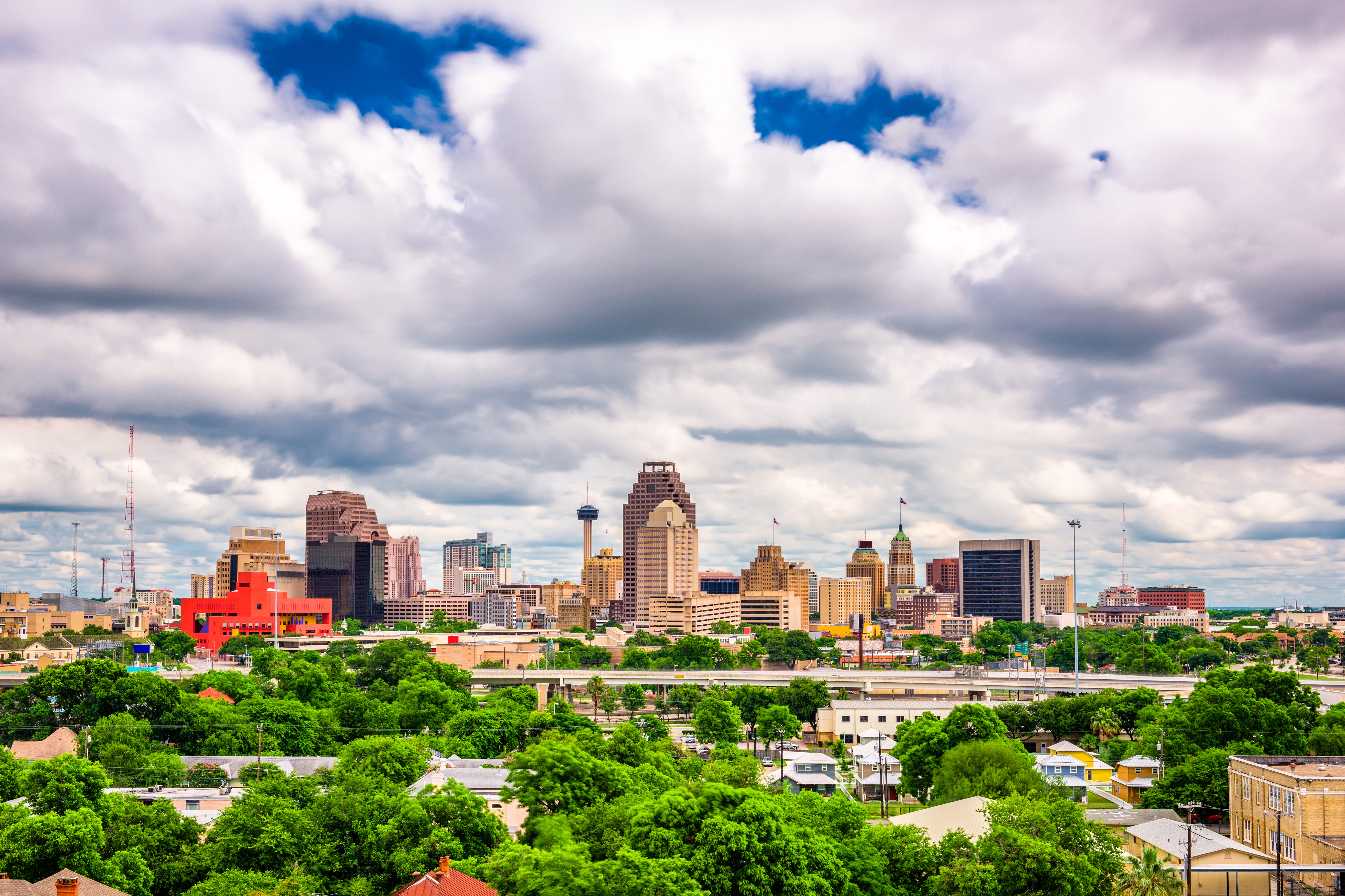 Downtown San Antonio skyline with lush greenery under cloudy skies.