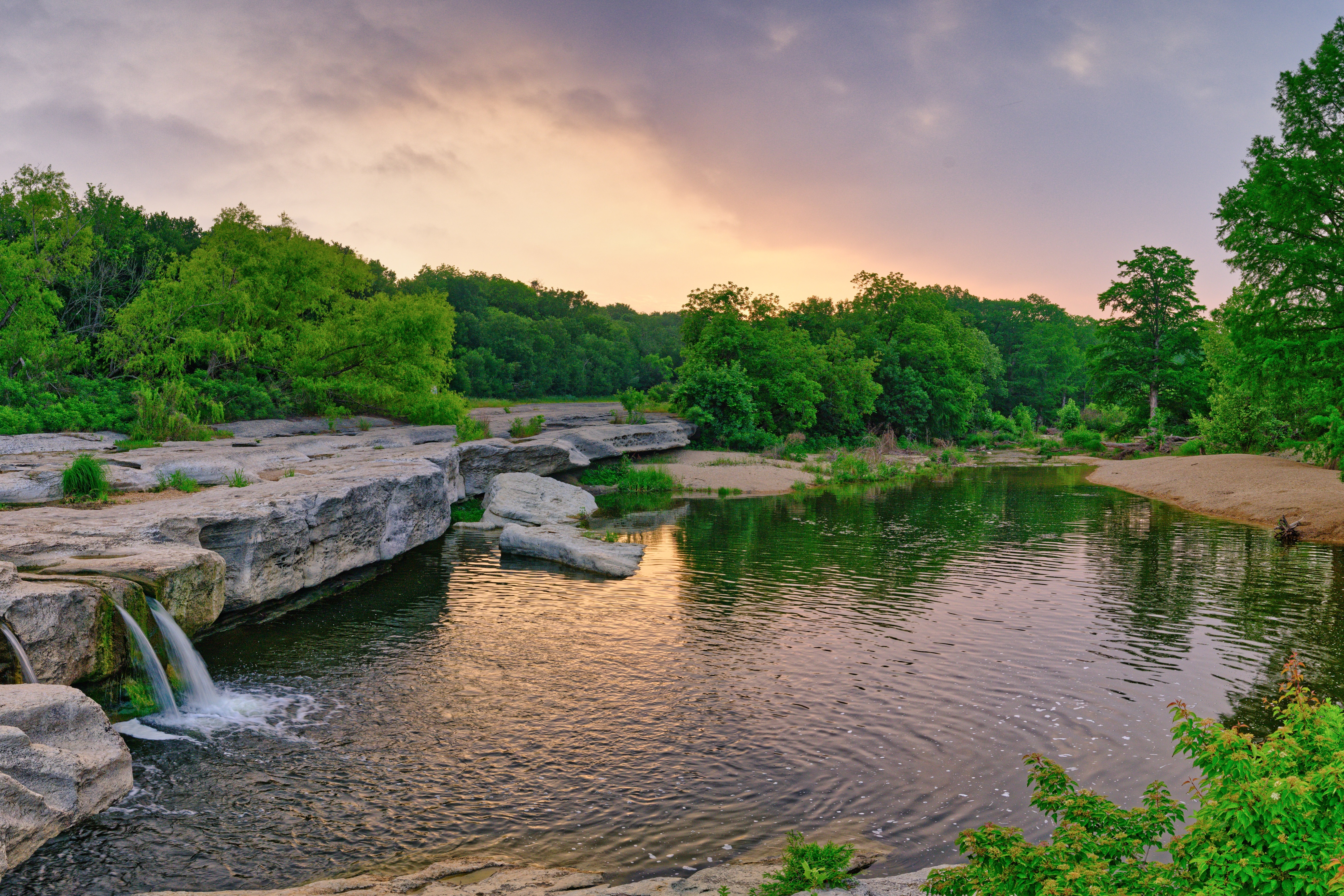 Sunrise at McKinney Falls State Park in Austin with a small waterfall, limestone ledges, and a calm pool.